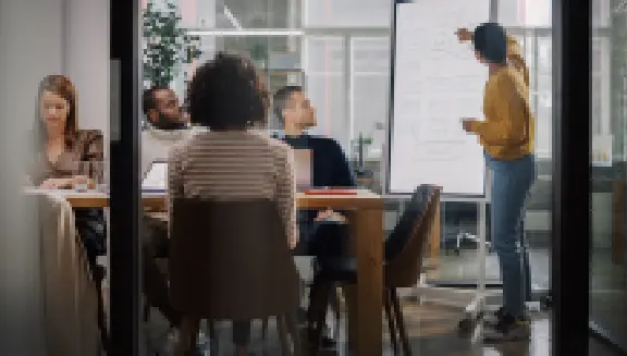 Transformative Team collaborating in an office as a presenter explains ideas on a whiteboard during a meeting.